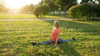 艺术体操运动员坐在纵向和横向分裂上。 在城市公园里伸展